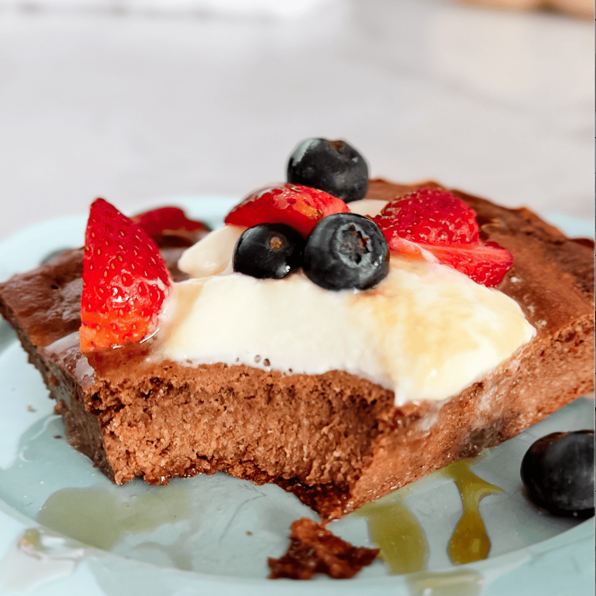 Chocolate cake slice with whipped cream, fresh strawberries, and blueberries on a decorative plate.