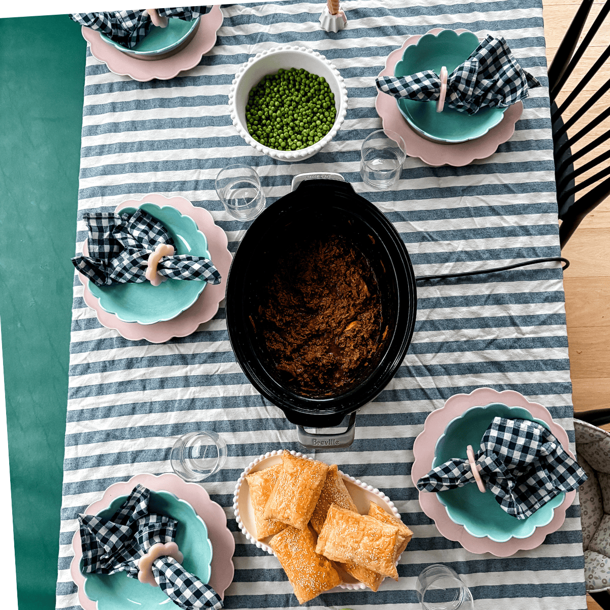 Overhead view of a dinner table with striped runner, pink and teal scalloped plates, peas, chocolate dessert, and pastries.